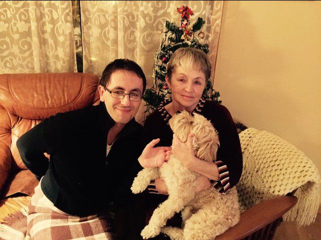 Two women smiling with a fluffy dog in a cozy living room.