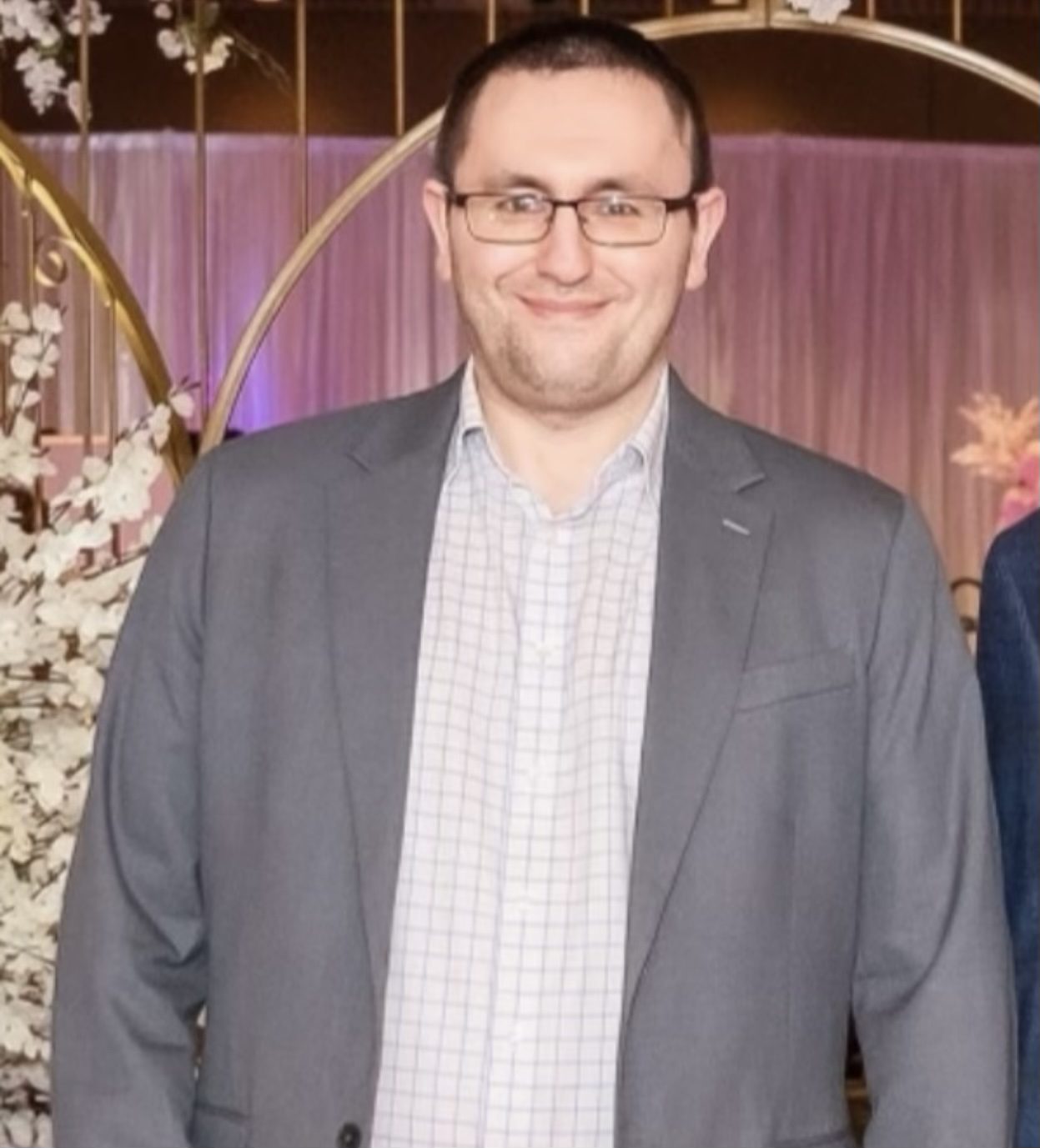 Man in glasses and gray jacket smiling at an event.