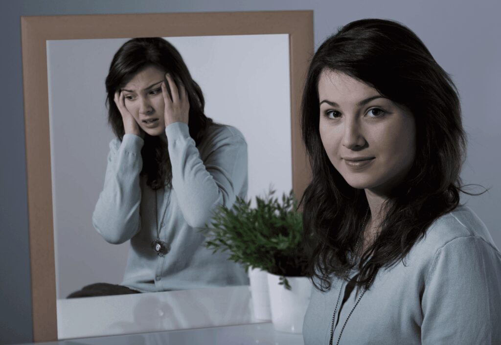 Two women, one in front and one reflected in a mirror, with a plant.
