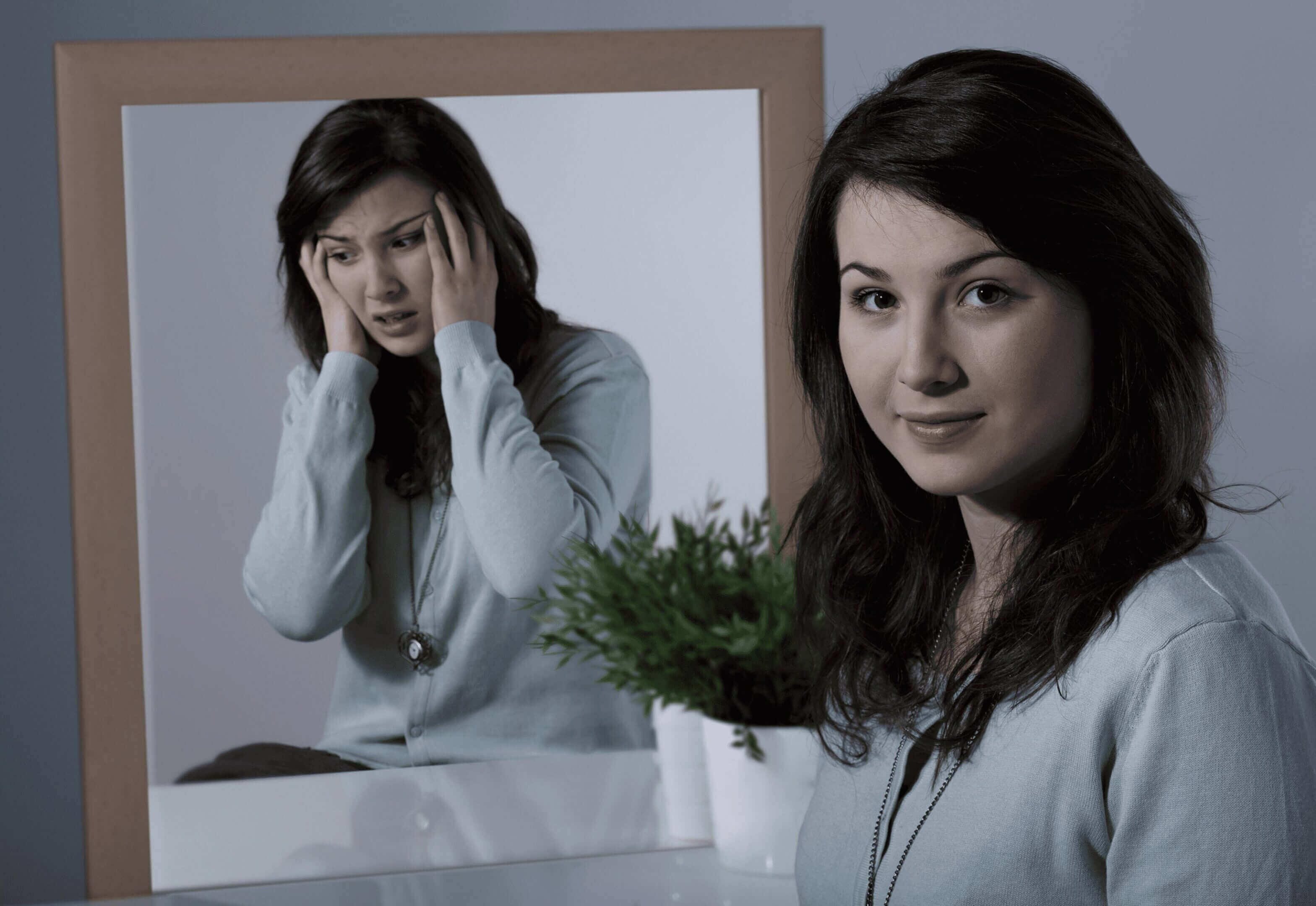 Two women, one in front and one reflected in a mirror, with a plant.